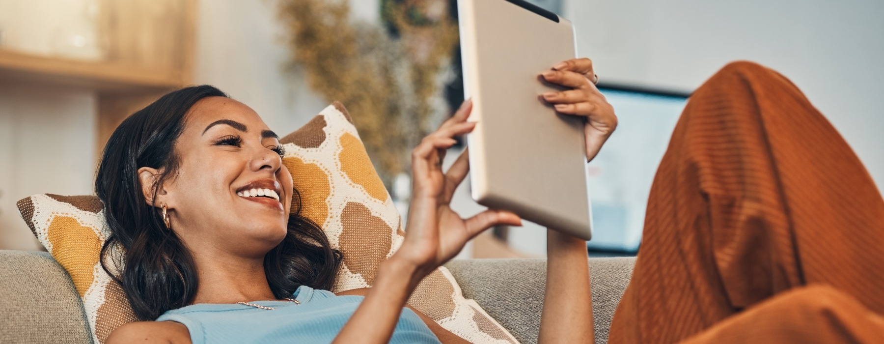 Resident relaxing on a couch while using a tablet, representing comfortable apartment living and positive resident experiences at Haven 8181.
